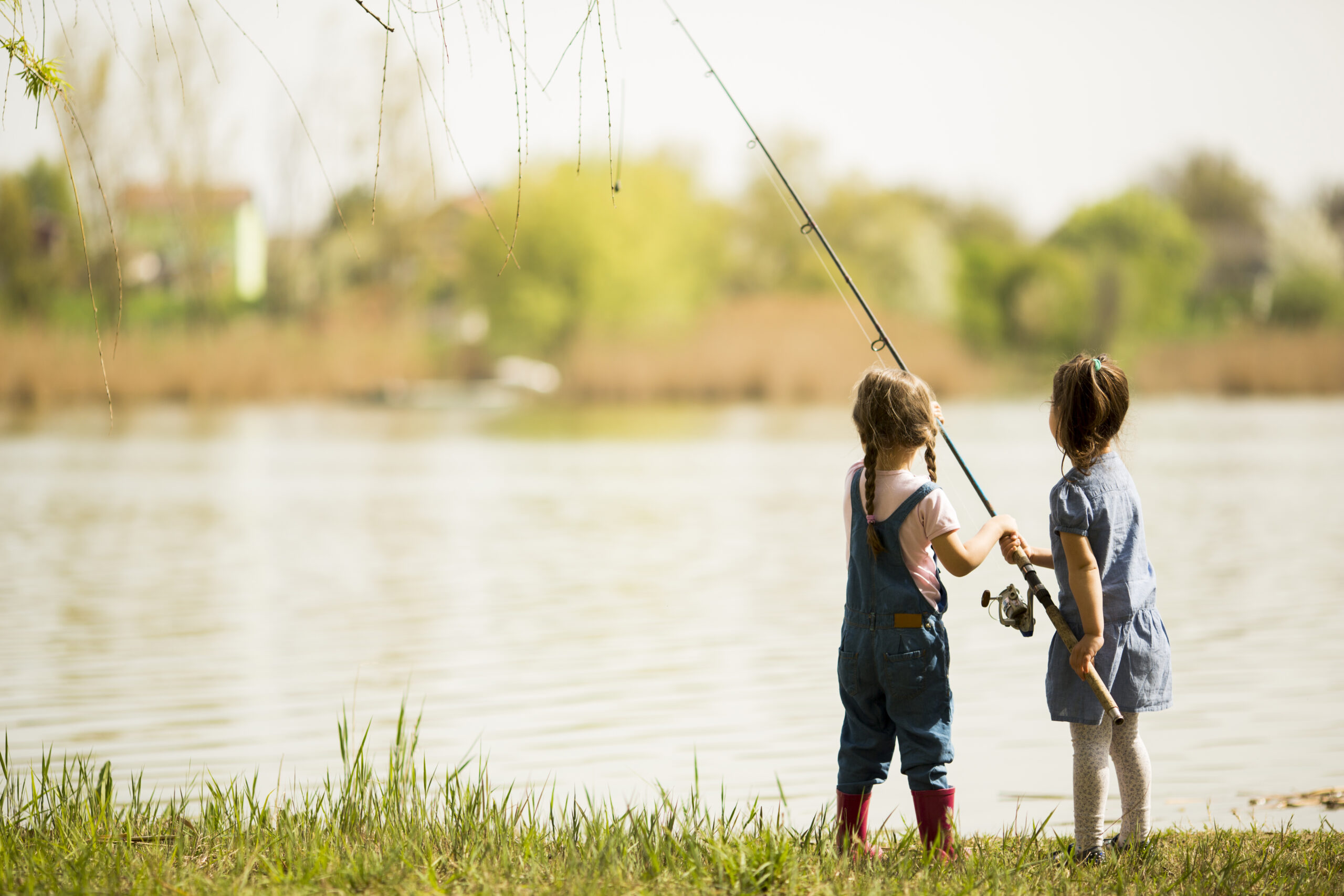 Two children fish by a lake on a sunny day.