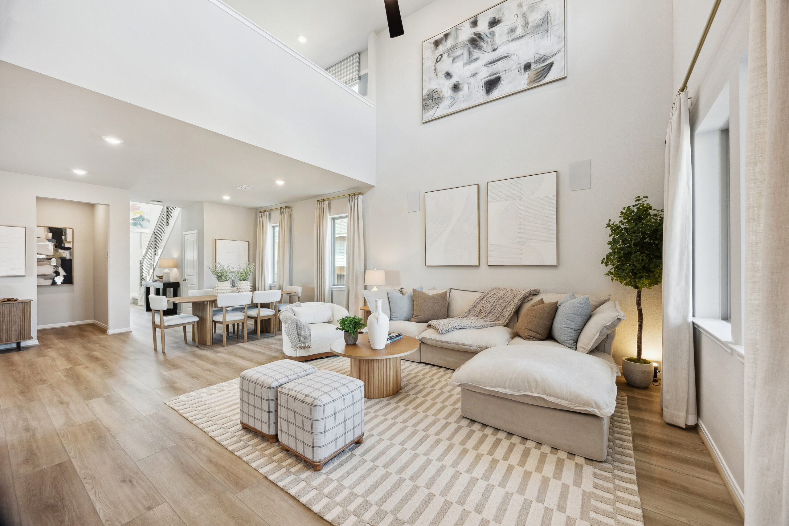 Modern living room with neutral tones, sectional sofa, ottomans, and large windows.