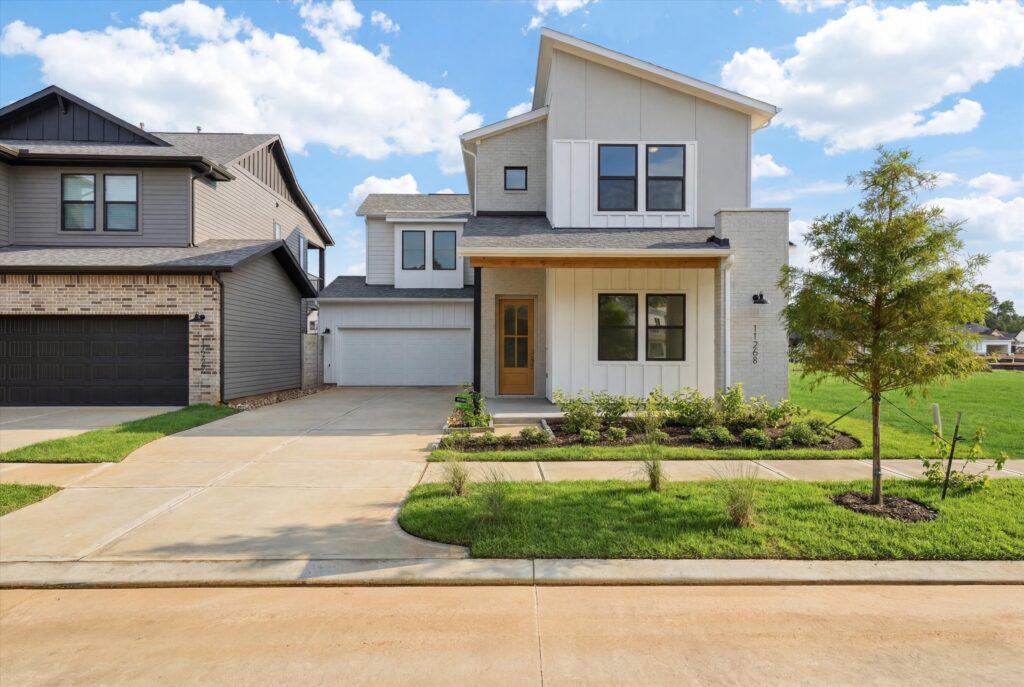Modern two-story house with white exterior, driveway, and front lawn under a blue sky.