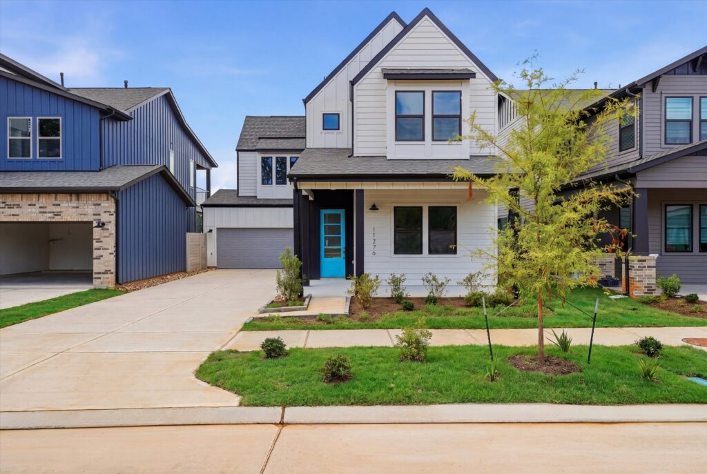 Modern two-story house with blue door, front yard, and driveway in a suburban neighborhood.