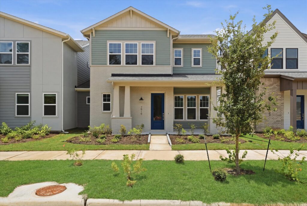 Two-story modern house with blue front door, small porch, and landscaped yard.