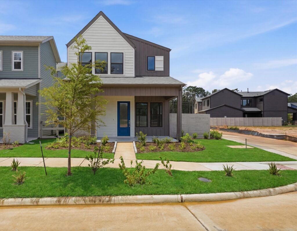 Modern two-story house with blue front door, lawn, and sidewalk under a clear sky.