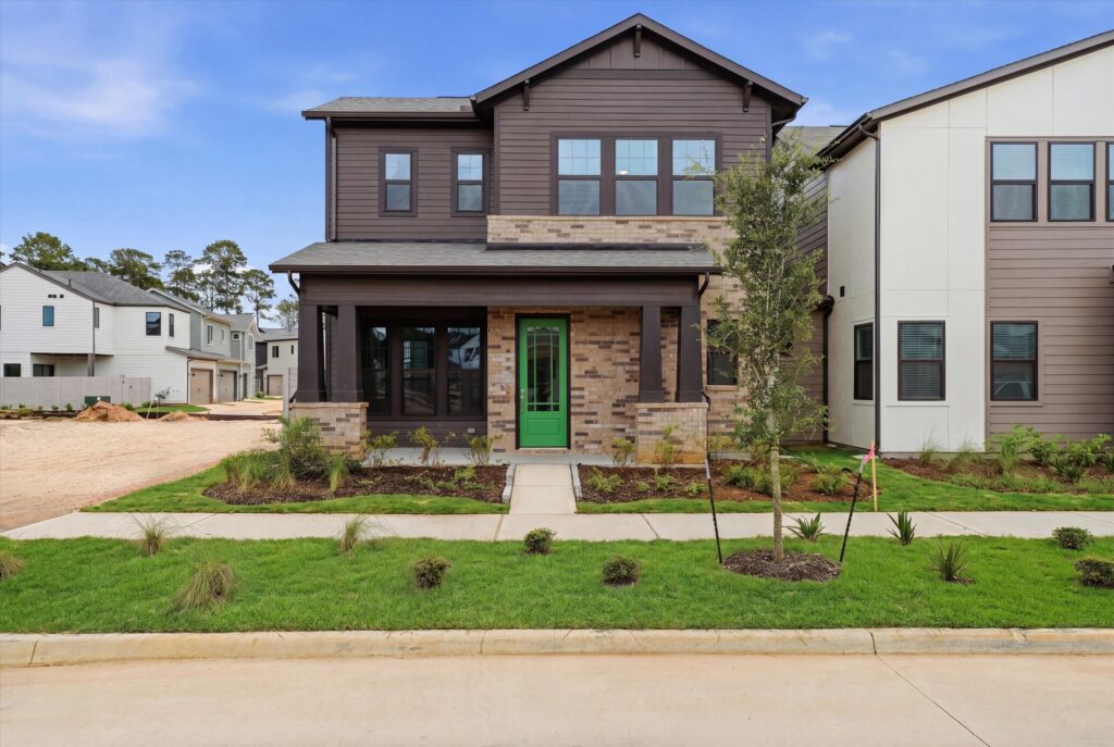 Two-story modern house with green front door, brick accents, and landscaped front yard.