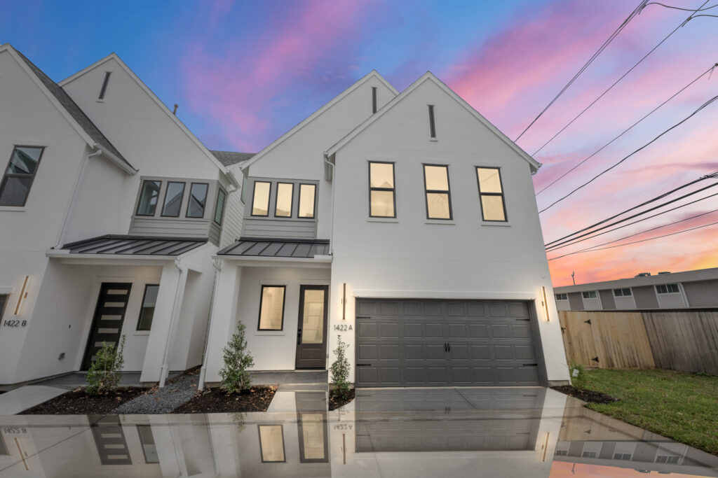 Modern white townhouse with a two-car garage at sunset, driveway and lawn in front new home built by Autograph Homes in Houston, TX.