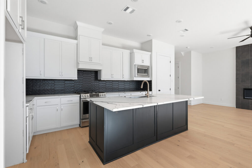 Modern kitchen by Autograph Homes with white cabinets, black tile, and marble island.