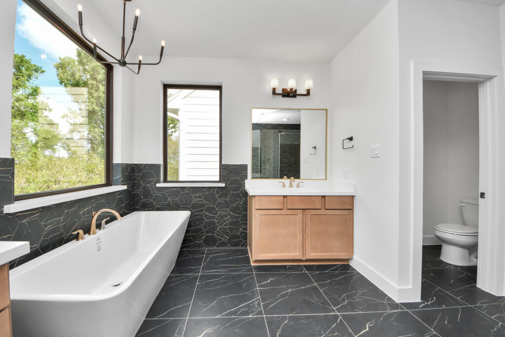 Modern bathroom with freestanding tub, wood vanity, large window, and black marble tile floor.