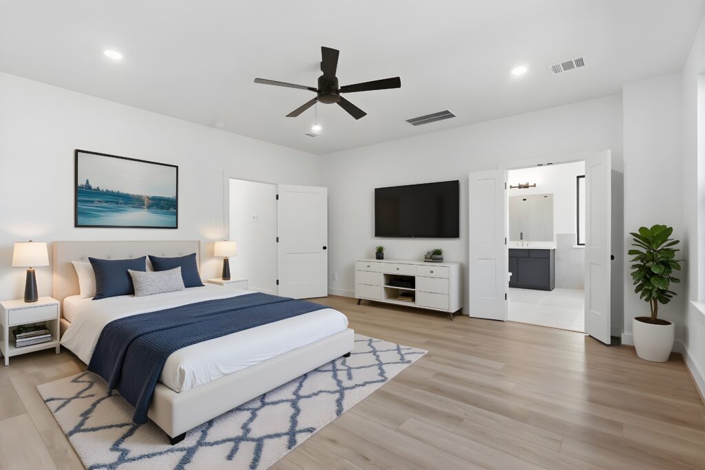 Autograph Homes modern bedroom in the Houston area with blue tones, large TV, and ensuite bathroom.