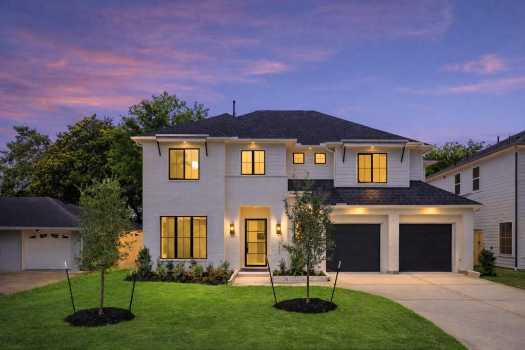 Two-story modern house with lit windows, a double garage, and a manicured front lawn at dusk new home built by Autograph Homes in Houston, TX.