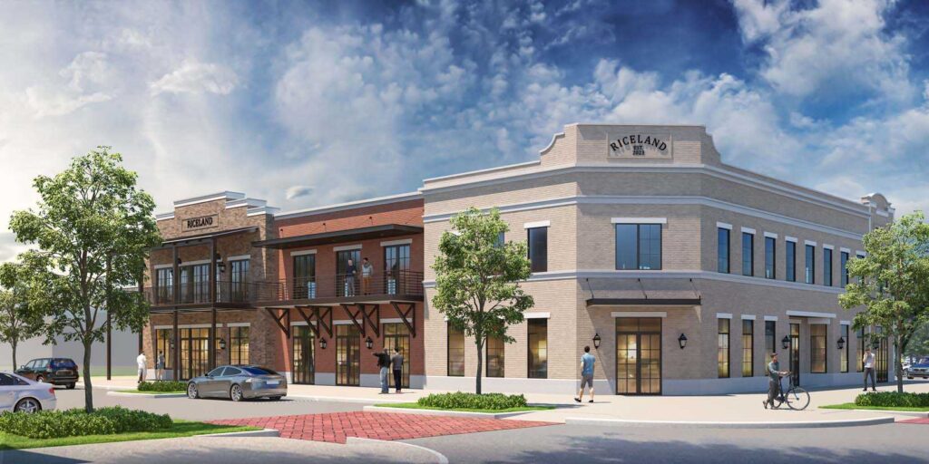 Two-story brick commercial building with large windows, trees, and people outside on sidewalk.