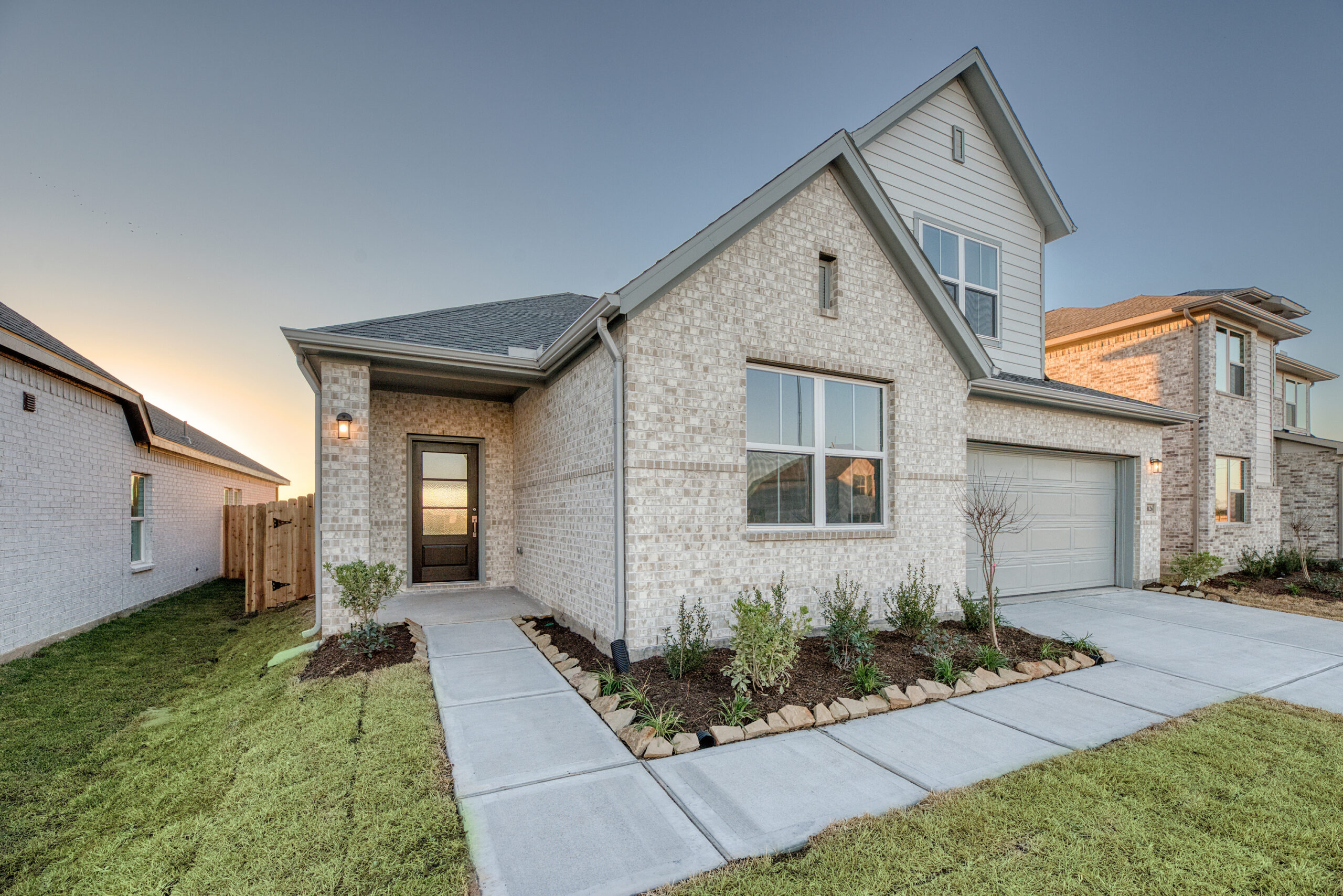 Modern two-story house with brick exterior, driveway, garage, and landscaped front yard.