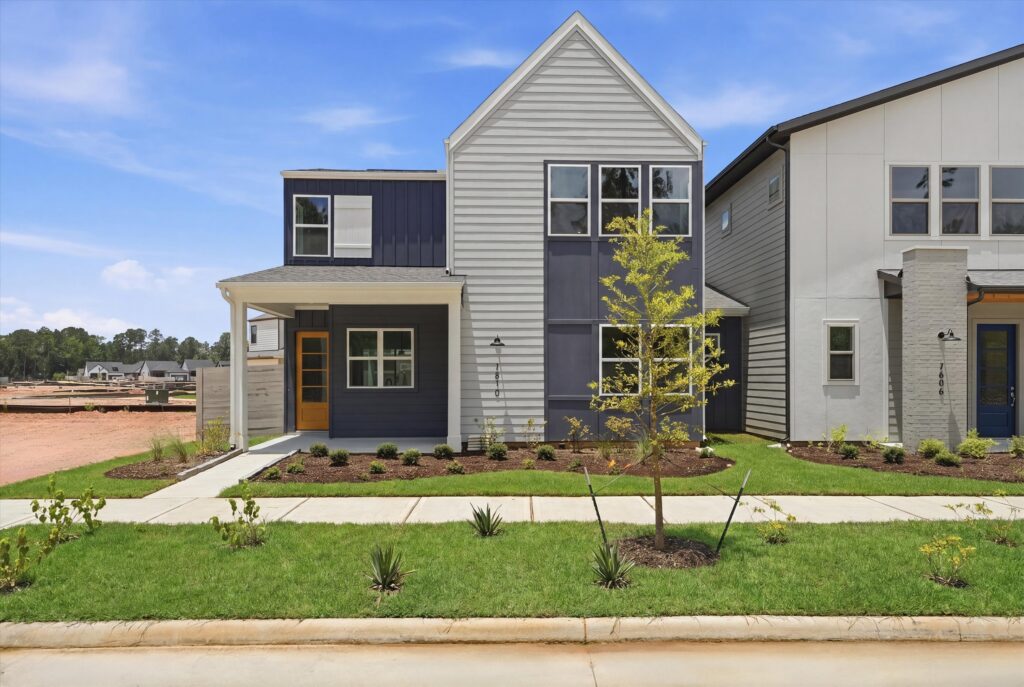Modern two-story house with gray siding, front porch, and small landscaped yard.