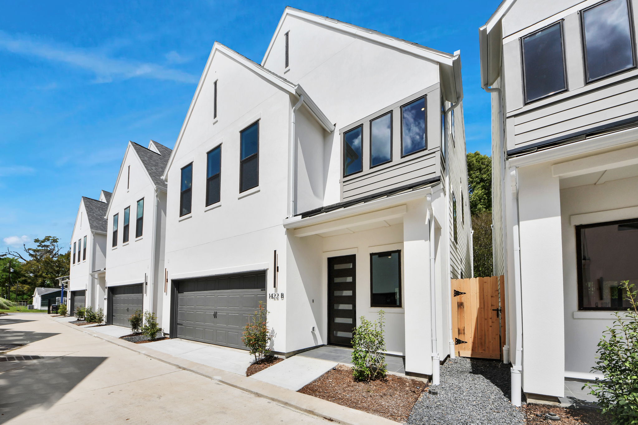 Row of modern white townhouses with dark garage doors on a sunny day.