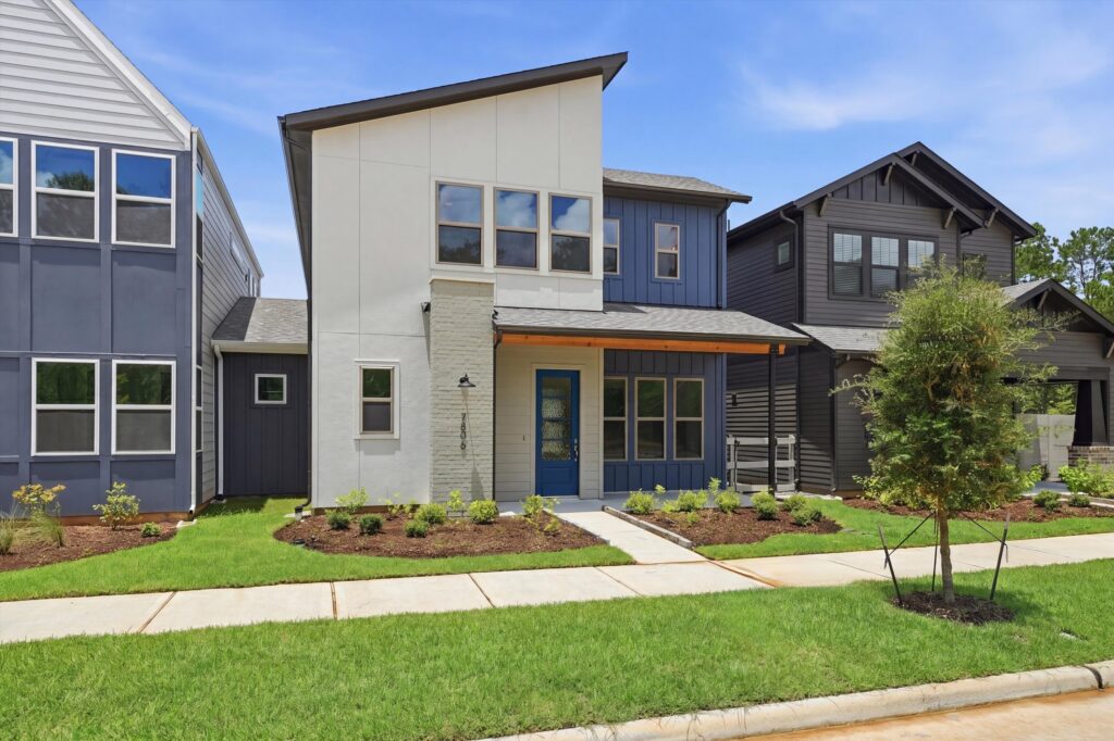 Modern two-story house with blue front door, landscaped yard, and sidewalk in front.